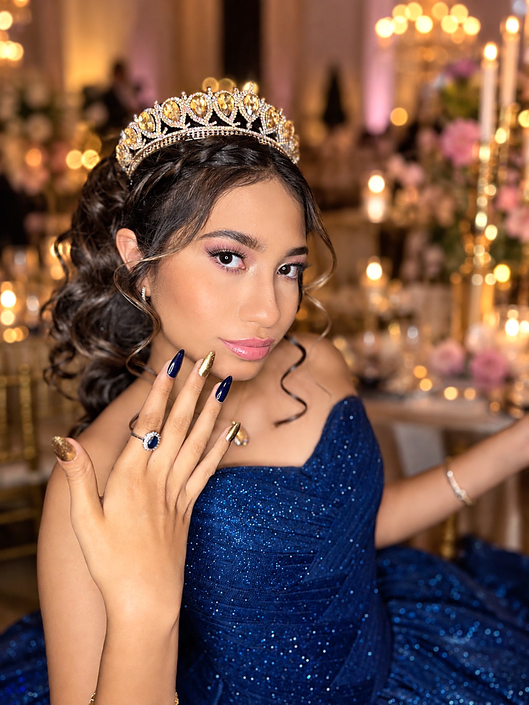 Quinceañera con vestido azul bordado, corona dorada y maquillaje rosado luminoso